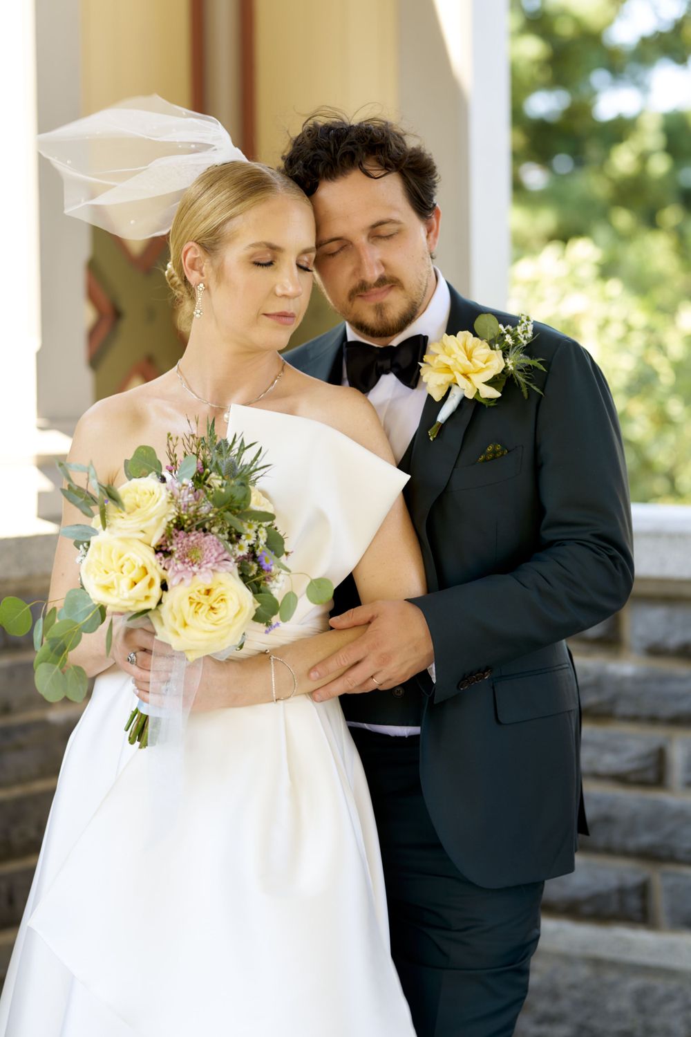 Tender wedding moment with bride holding yellow bouquet as couple poses on stone steps.