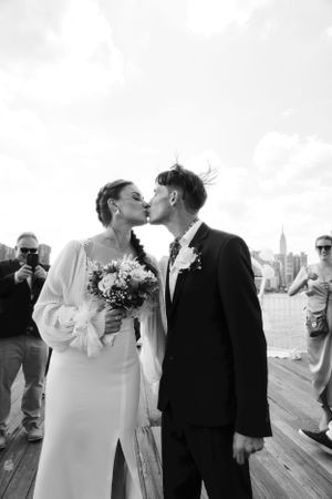 Black and white wedding portrait on a waterfront deck with city skyline in background.
