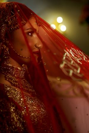 A close-up artistic shot through a red veil with sparkling embellishments and golden lighting.
