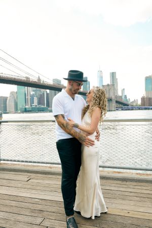 A couple shares an intimate moment on a waterfront deck with the New York City skyline in the background.