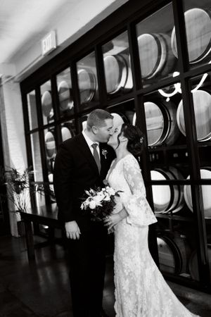Romantic black and white portrait of newlyweds sharing a kiss in front of a decorative wall.