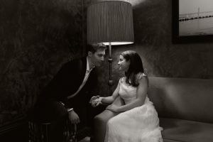 Intimate black and white portrait of couple sitting together on couch under lamp light.