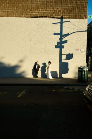 Three silhouettes cast dramatic shadows against a light wall with a utility pole in an urban setting during sunset.