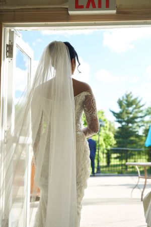 A row of elegant white wedding dresses hanging on display inside a venue near an exit sign.