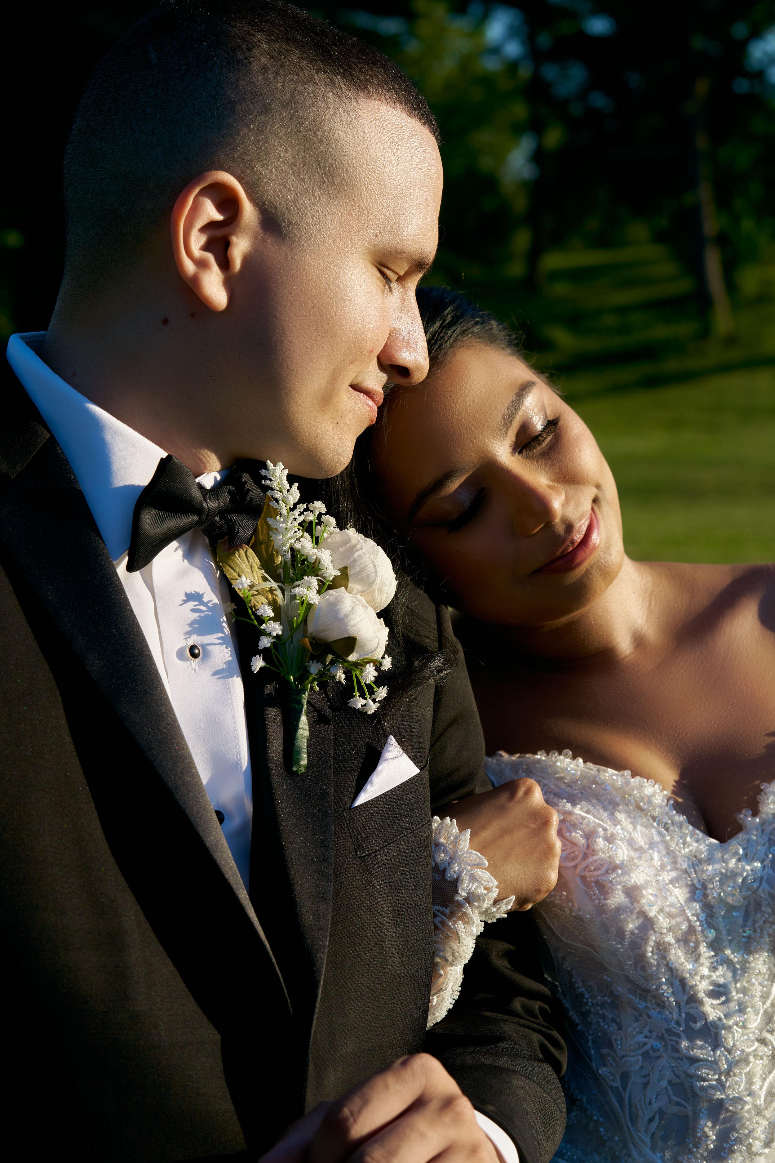 A romantic wedding portrait showing a tender moment between newlyweds in formal attire outdoors.