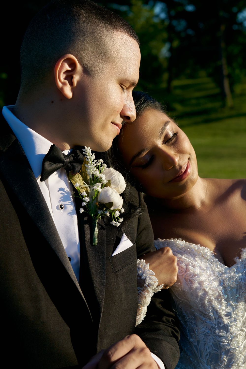 A romantic wedding portrait showing a tender moment between newlyweds in formal attire outdoors.