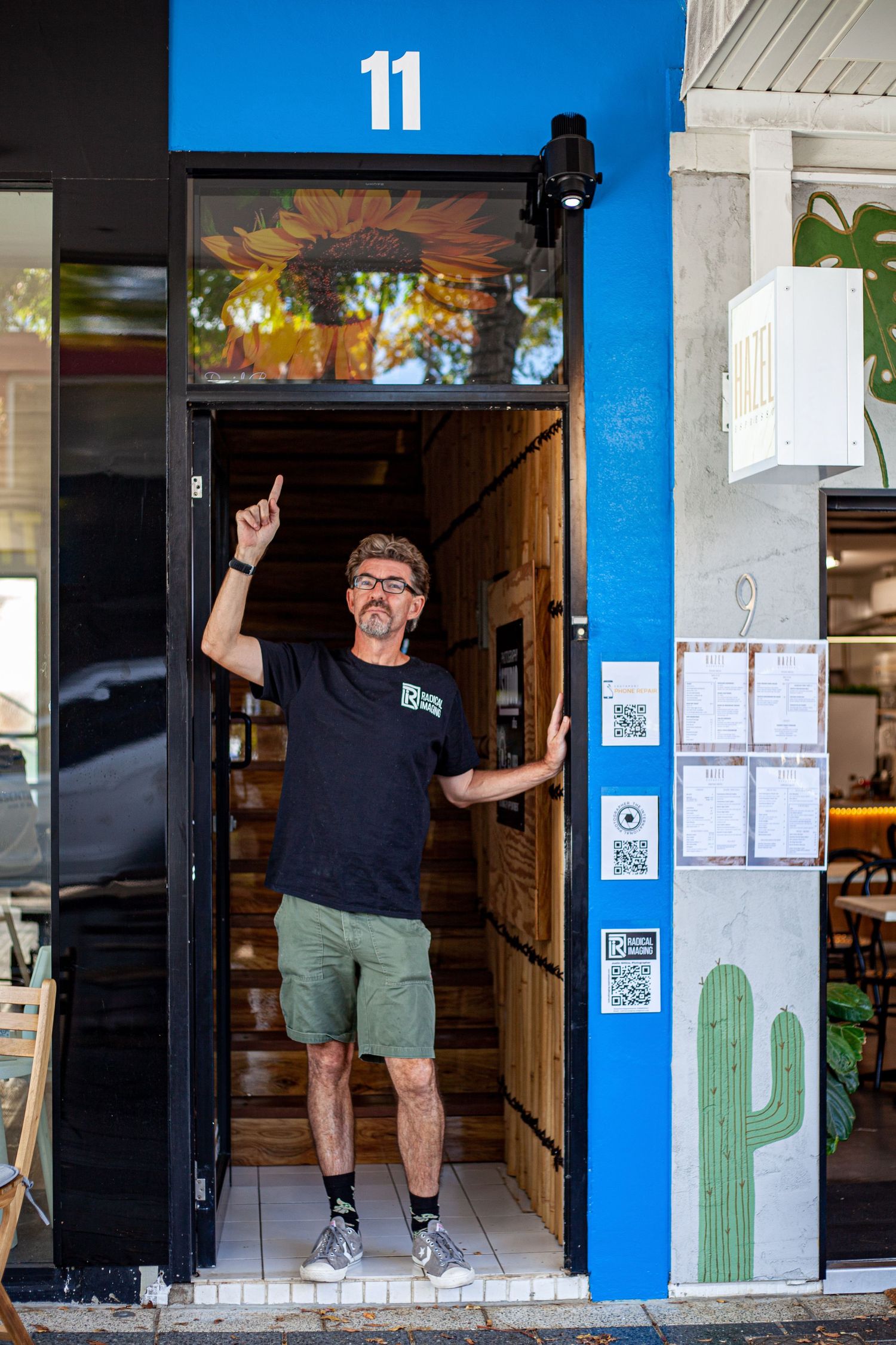 Person gesturing in doorway of business with bright blue exterior and cactus mural.