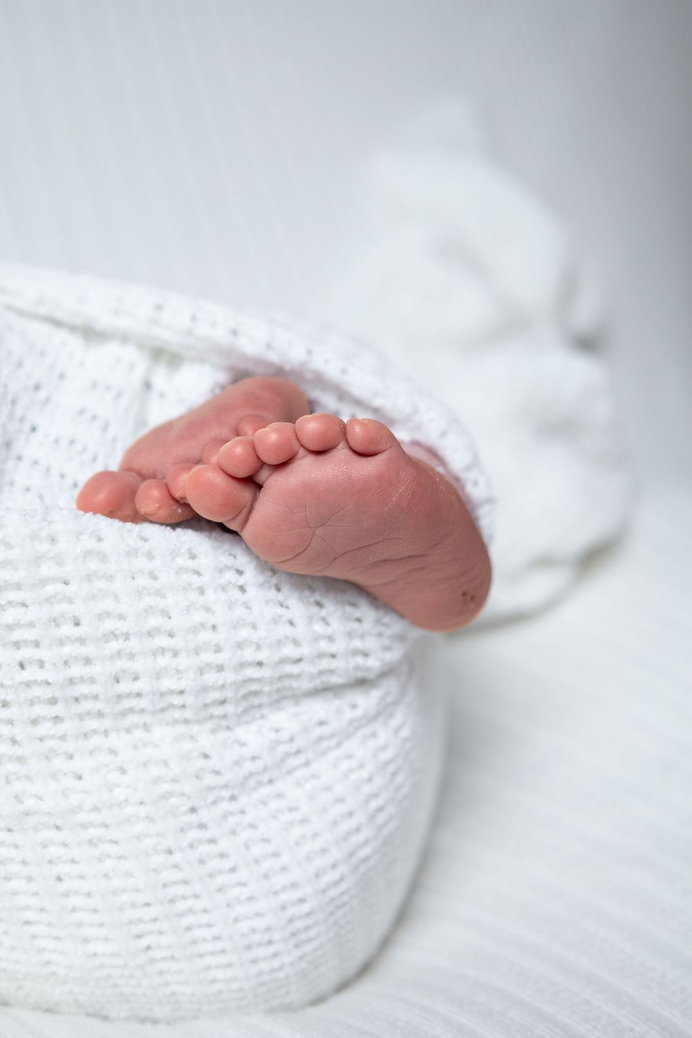Close-up of tiny newborn baby feet peeking out from white knit blanket in basket.