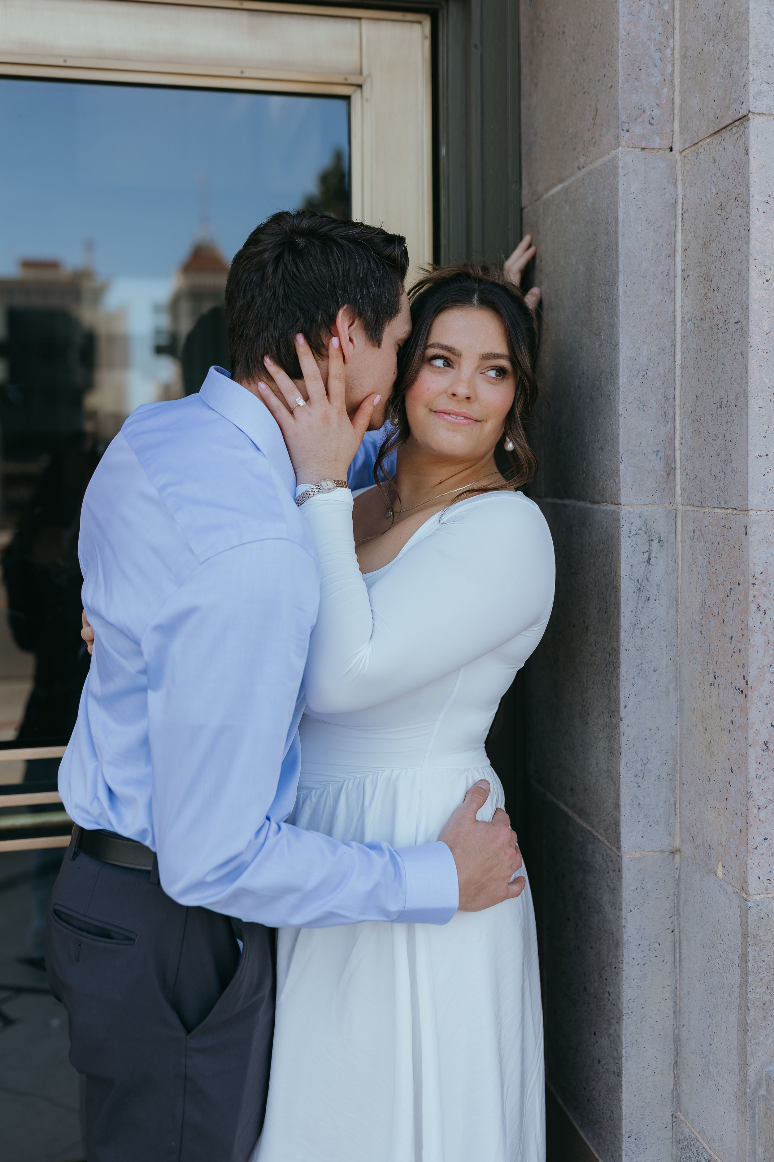 couple embracing outdoors beside a building, sharing an intimate moment during a engagement portrait session