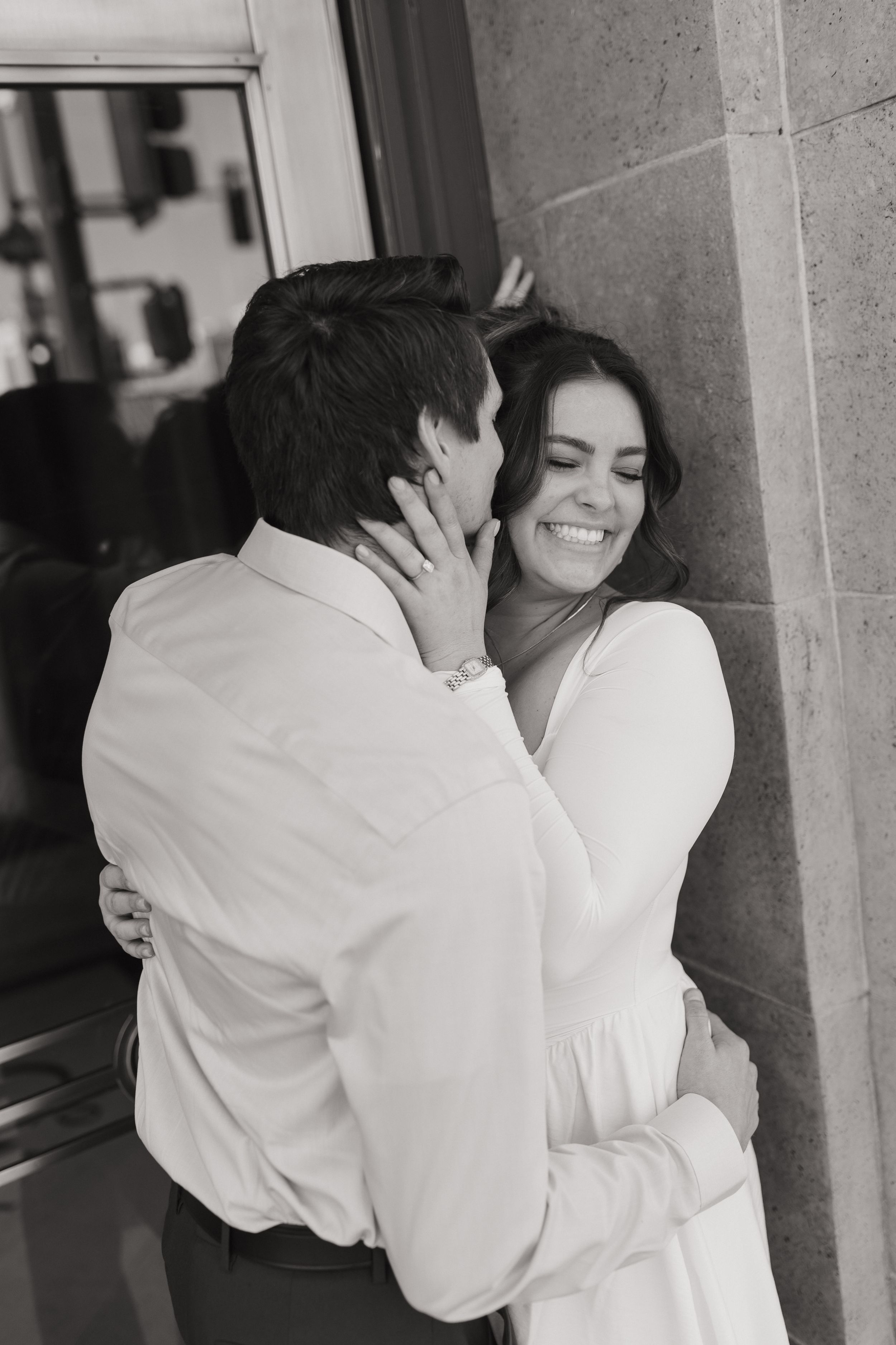 couple embracing outdoors beside a building, sharing an intimate moment during a engagement portrait session
