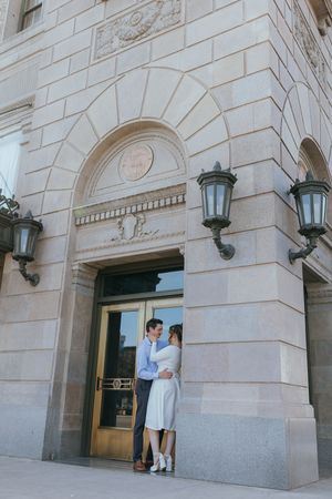 couple embracing outdoors beside a building, sharing an intimate moment during a engagement portrait session in front of the Grand 1401