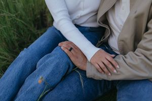 close up of a couple sitting together in grassy field, with their hands resting on each other's legs during a couples portrait session