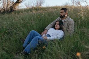couple relaxing together in tall grass during an outdoor couples portrait session, with one partner leaning back against the other