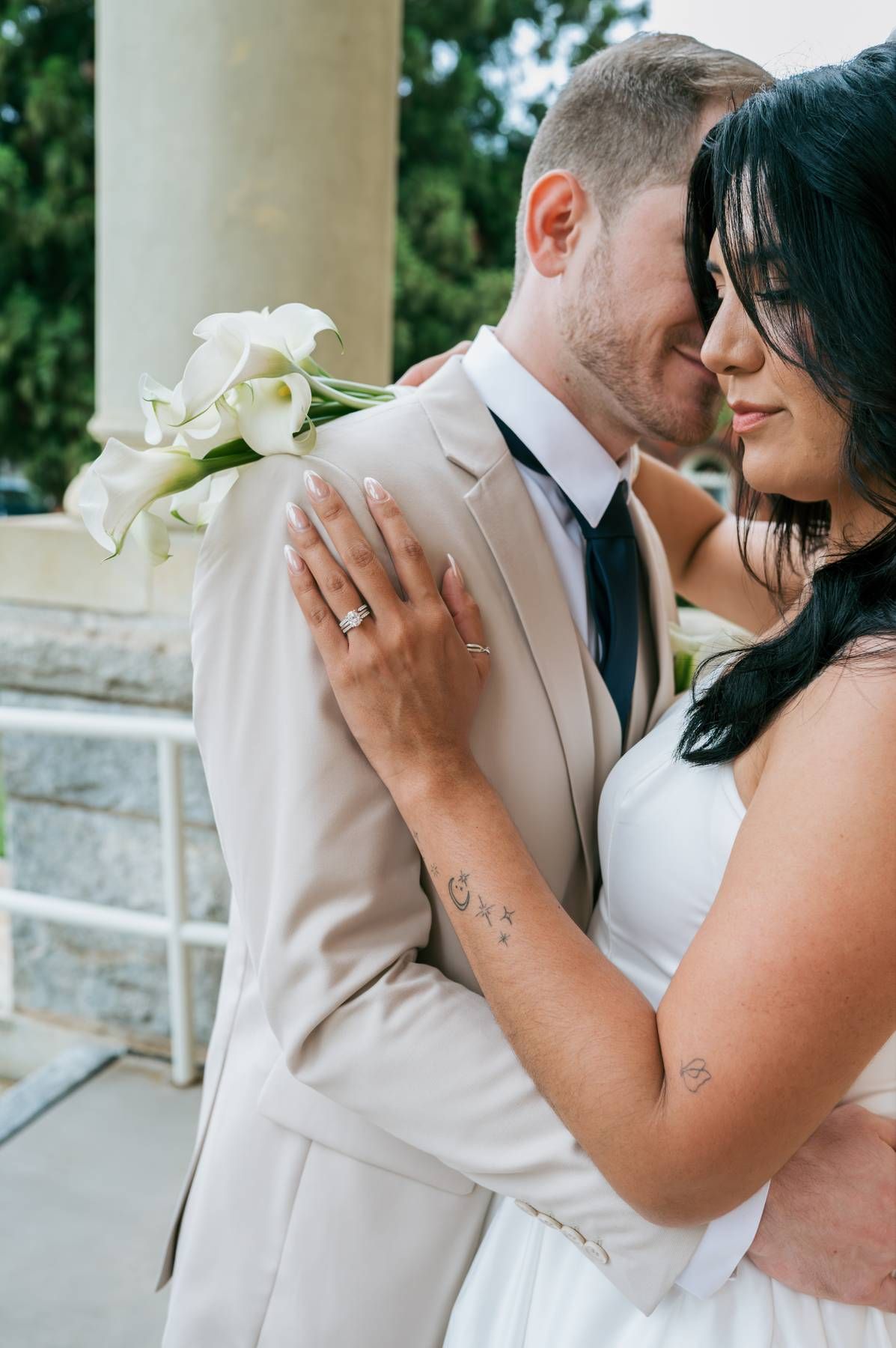 Bride and groom in intimate embrace holding white calla lily bouquet near stone columns in North Carolina