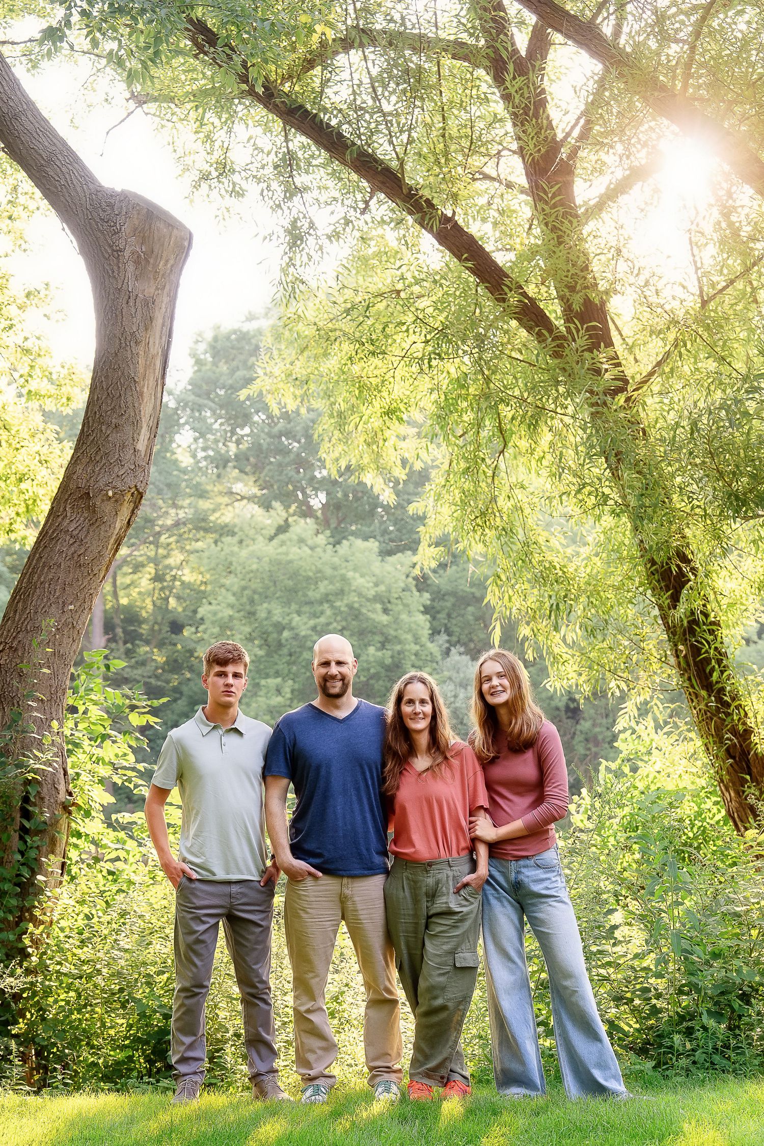 Family of 4 standing in front of trees with the sun behind them - shot by Milwaukee family photographer Rachel Dickman