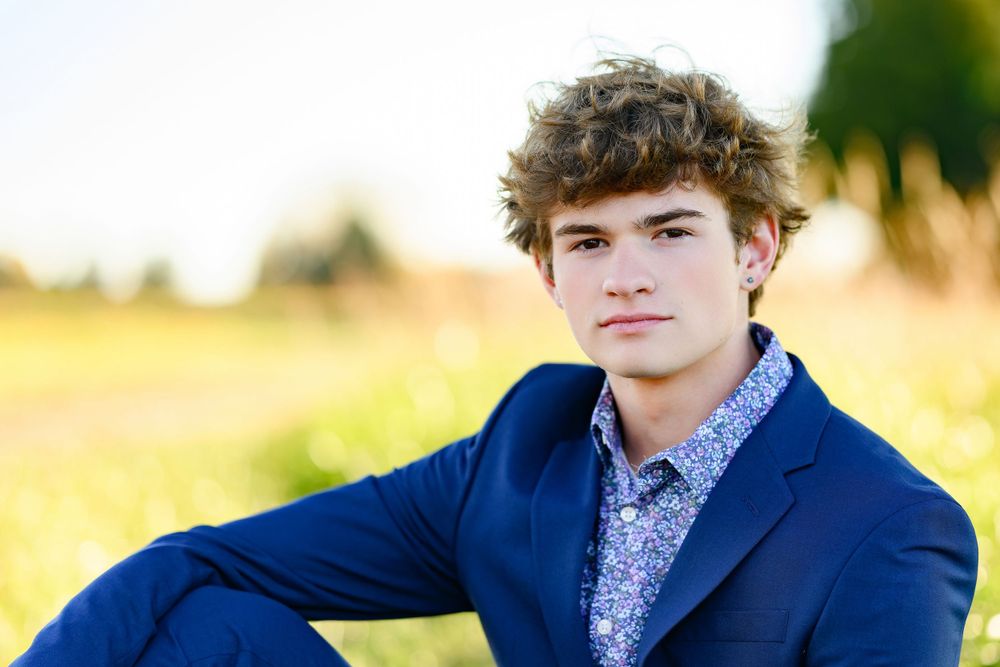 Outdoor portrait shot with someone wearing a navy blazer and patterned shirt against blurred fall foliage.