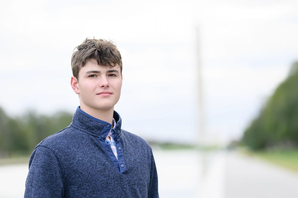 Someone in blue quarter-zip sweater poses outdoors with white architectural elements in background.