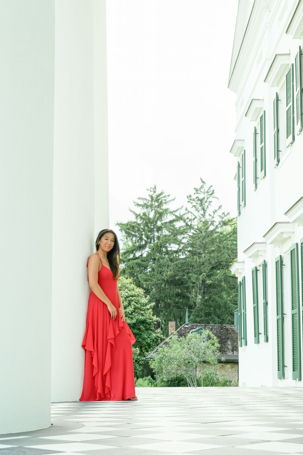 A woman in a flowing red dress poses elegantly on a white columned porch in an artistic photoshoot series.