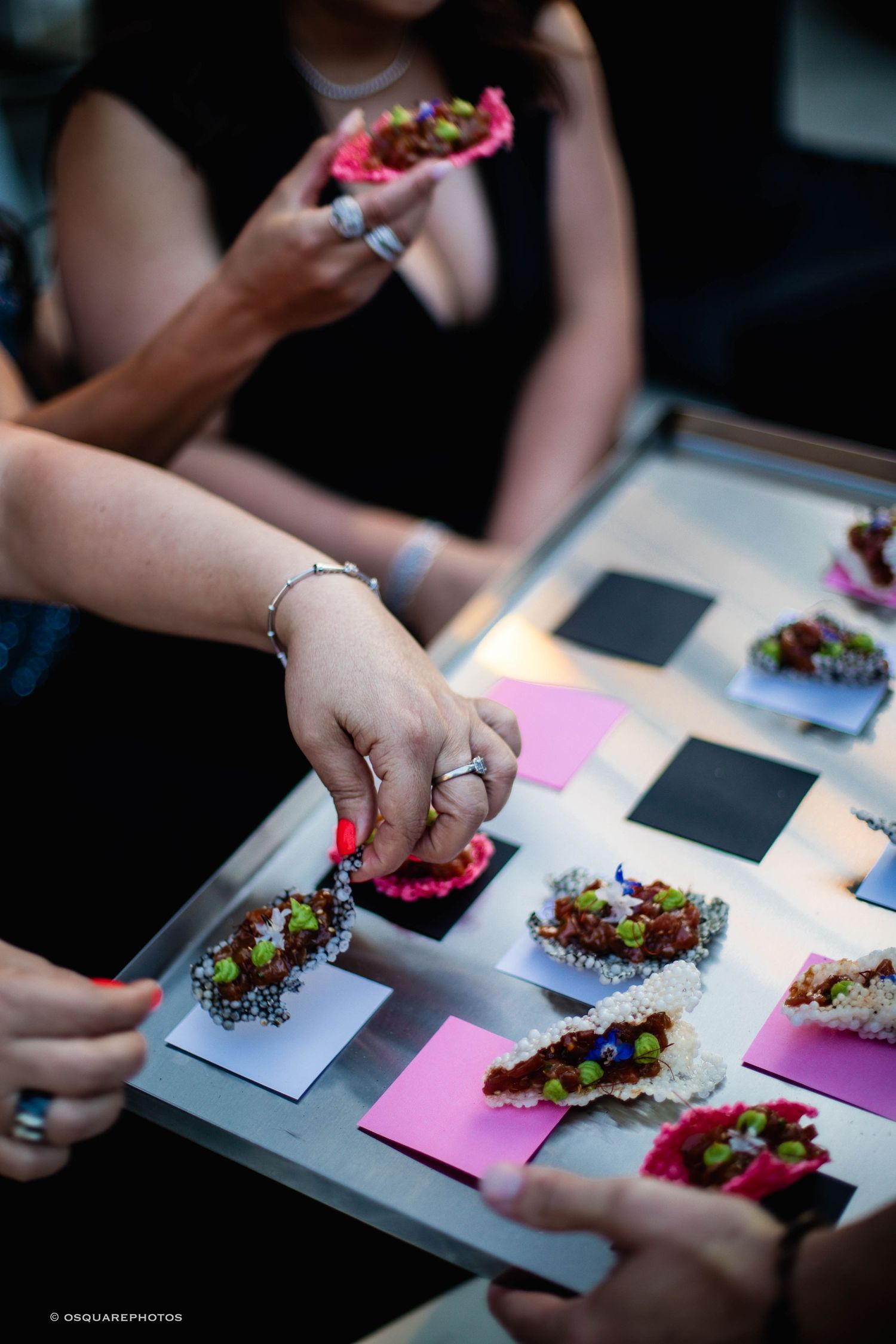 Hands arrange delicate floral arrangements on black and pink cards during a creative workshop session.