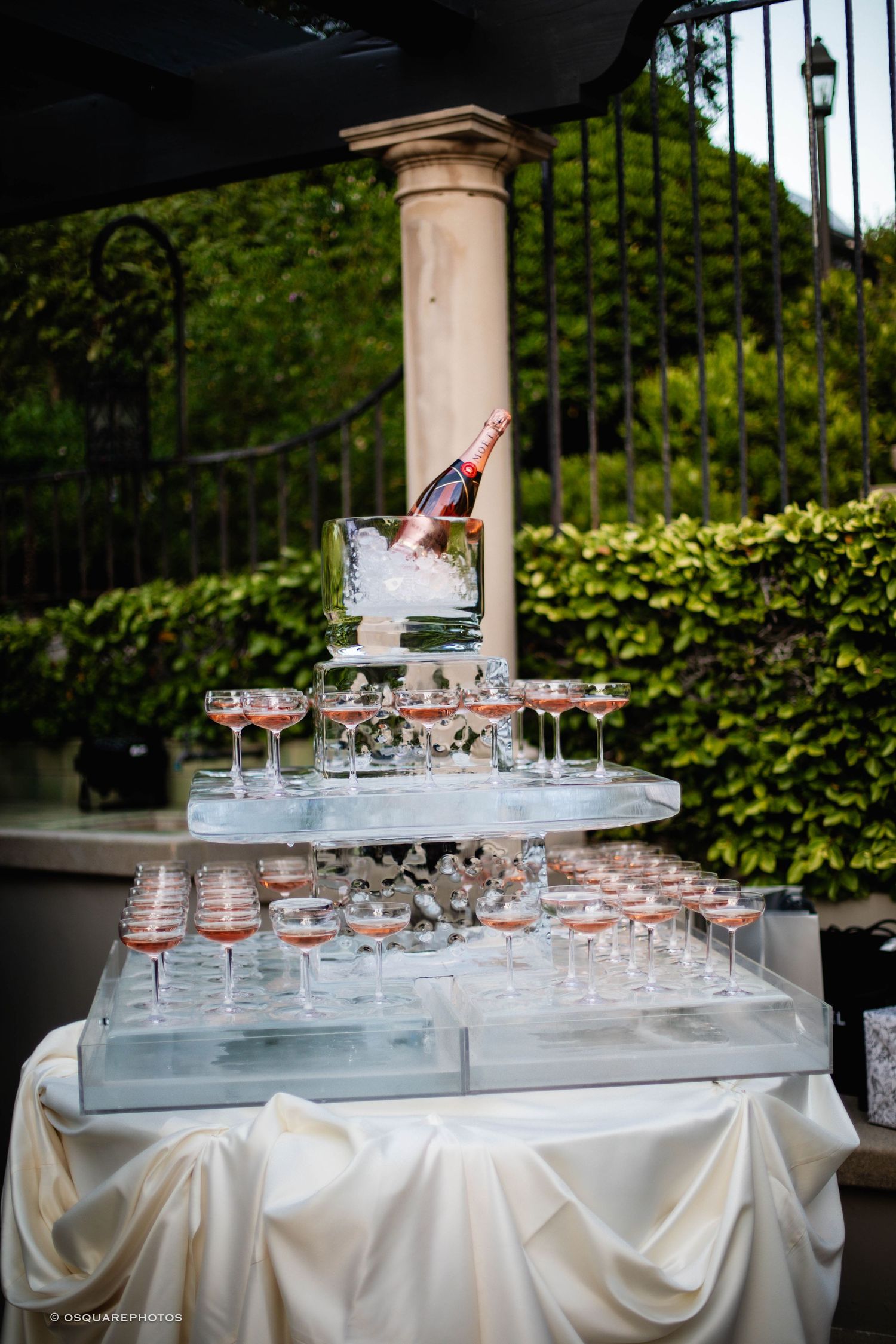 Elegant champagne tower display with crystal glasses arranged on a white draped table against a garden backdrop.