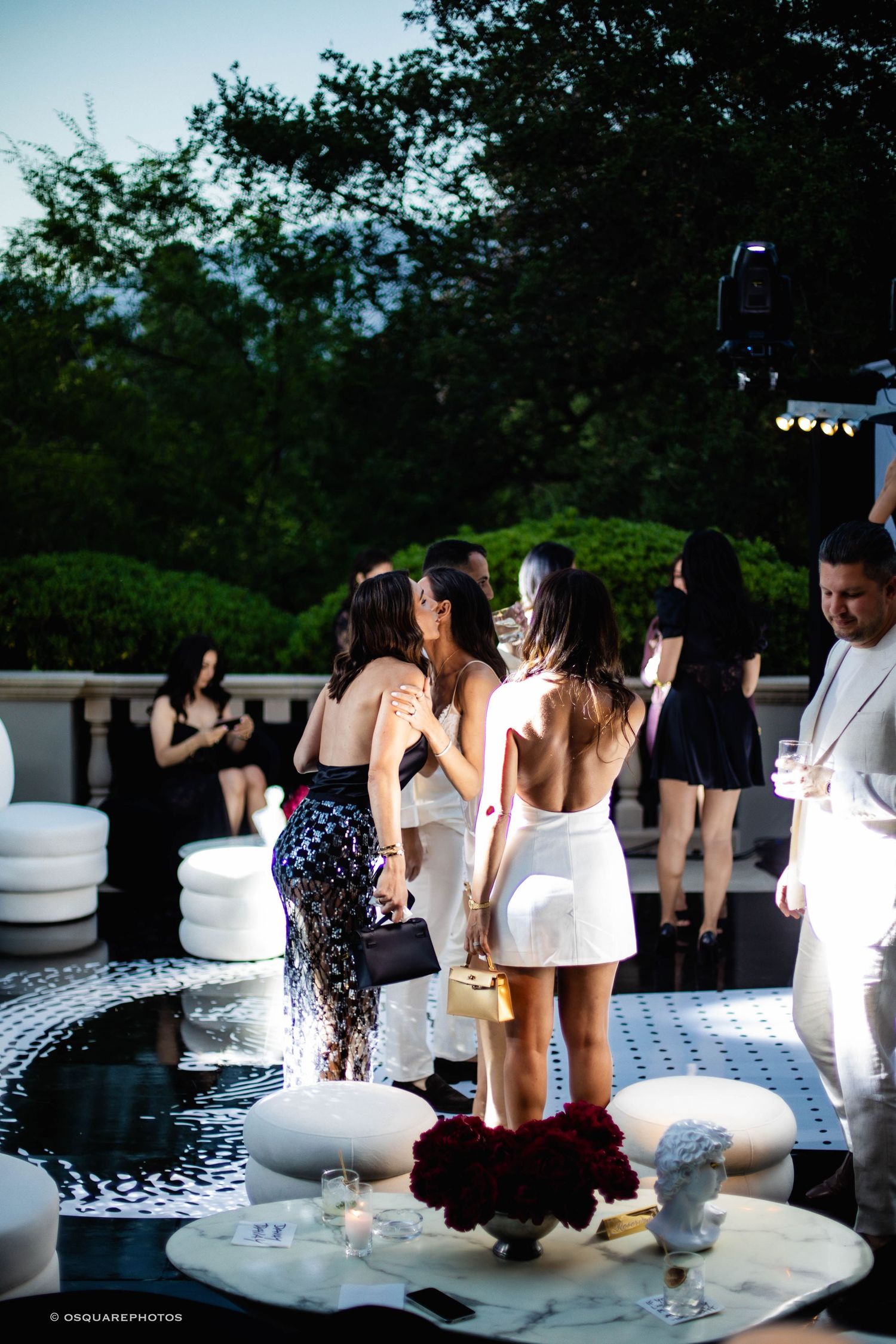 People gather around illuminated white seating at an outdoor nighttime party venue.