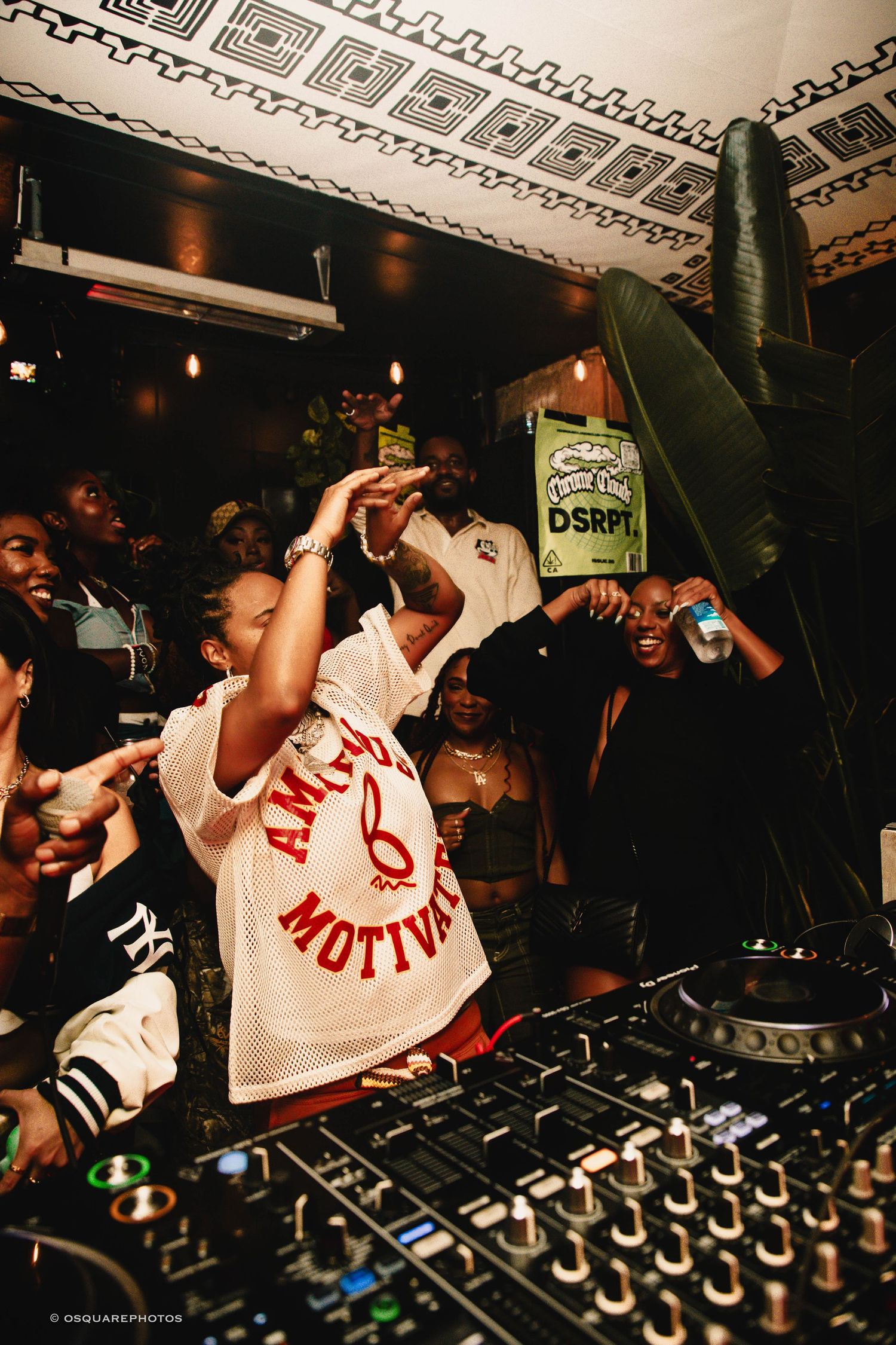 DJs perform at an energetic nightclub event with a crowd gathering around the mixing equipment.