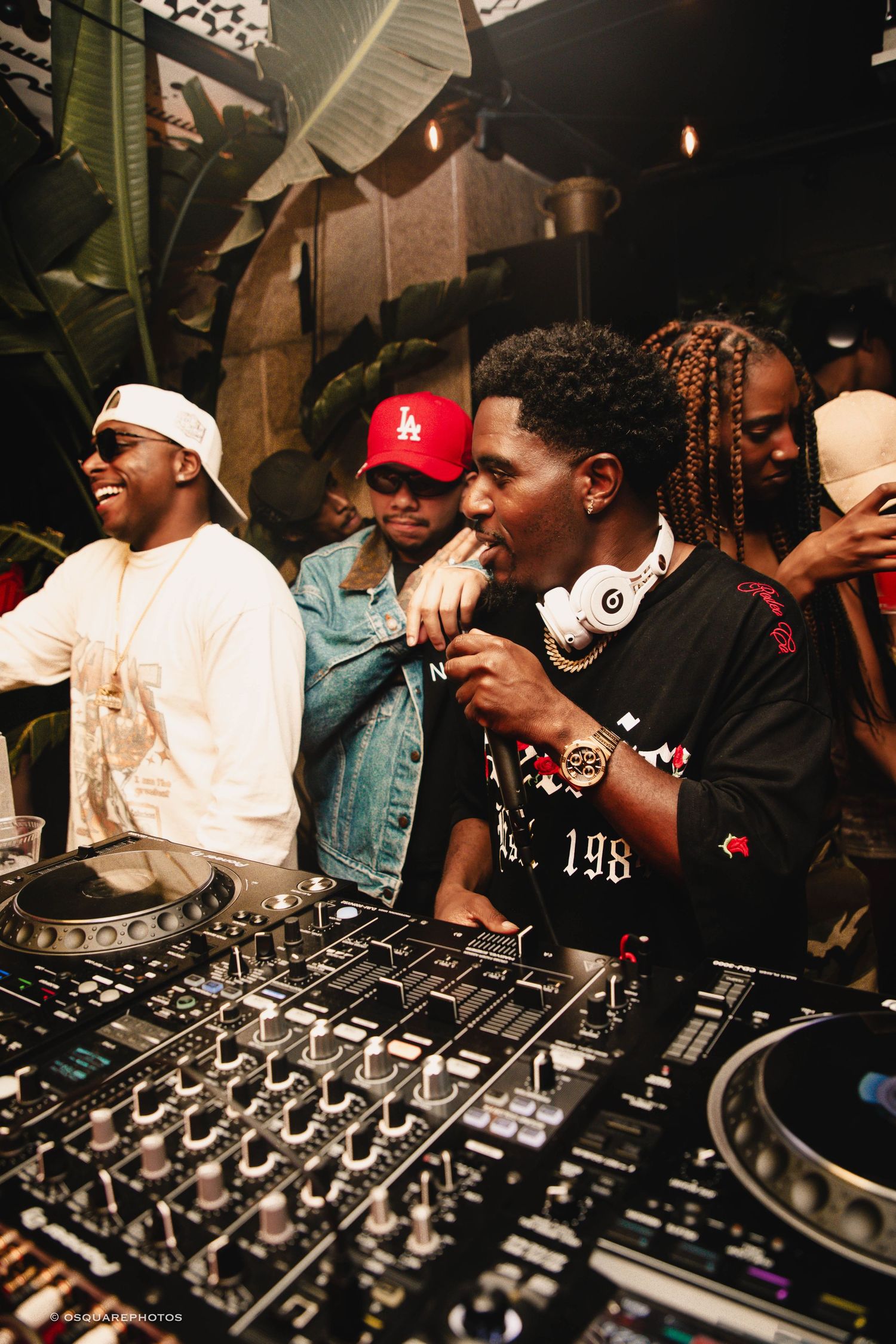 Group of performers energetically working the DJ equipment at a crowded nightclub party.