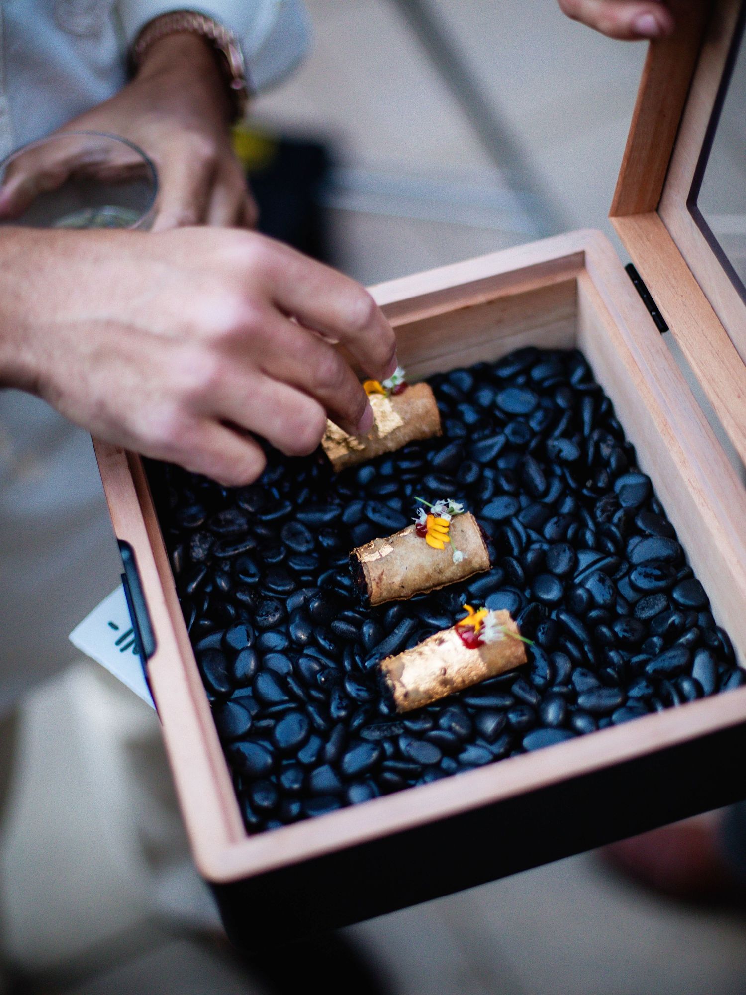 A series of wooden boxes filled with dark coffee beans show a roll being placed on top of the beans.