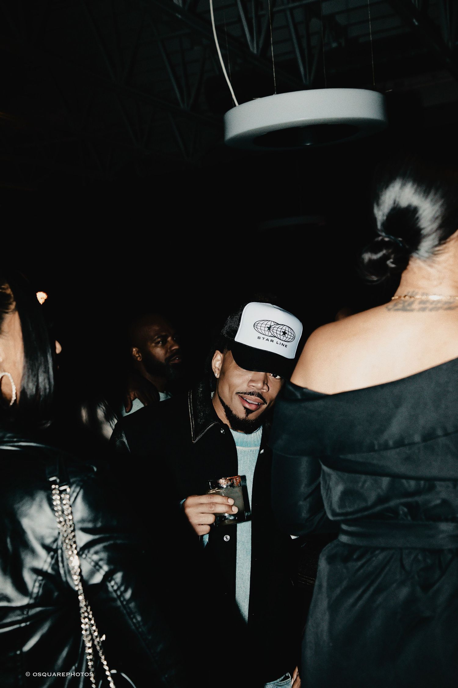 A dark nightclub scene showing people in black clothing and accessories with silver chain details.