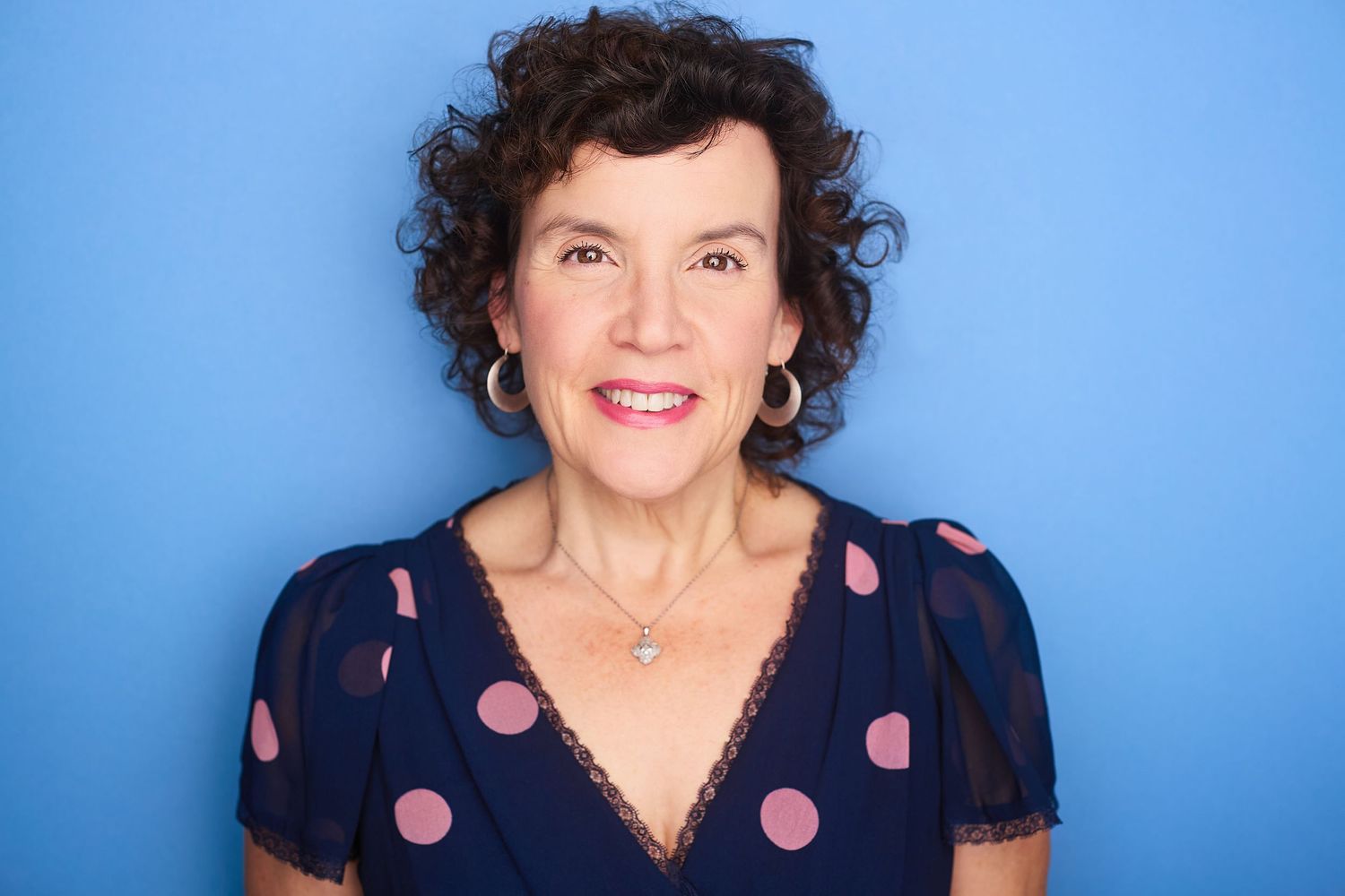Corporate NYC headshot of a woman in a polkadot shirt against a blue background.