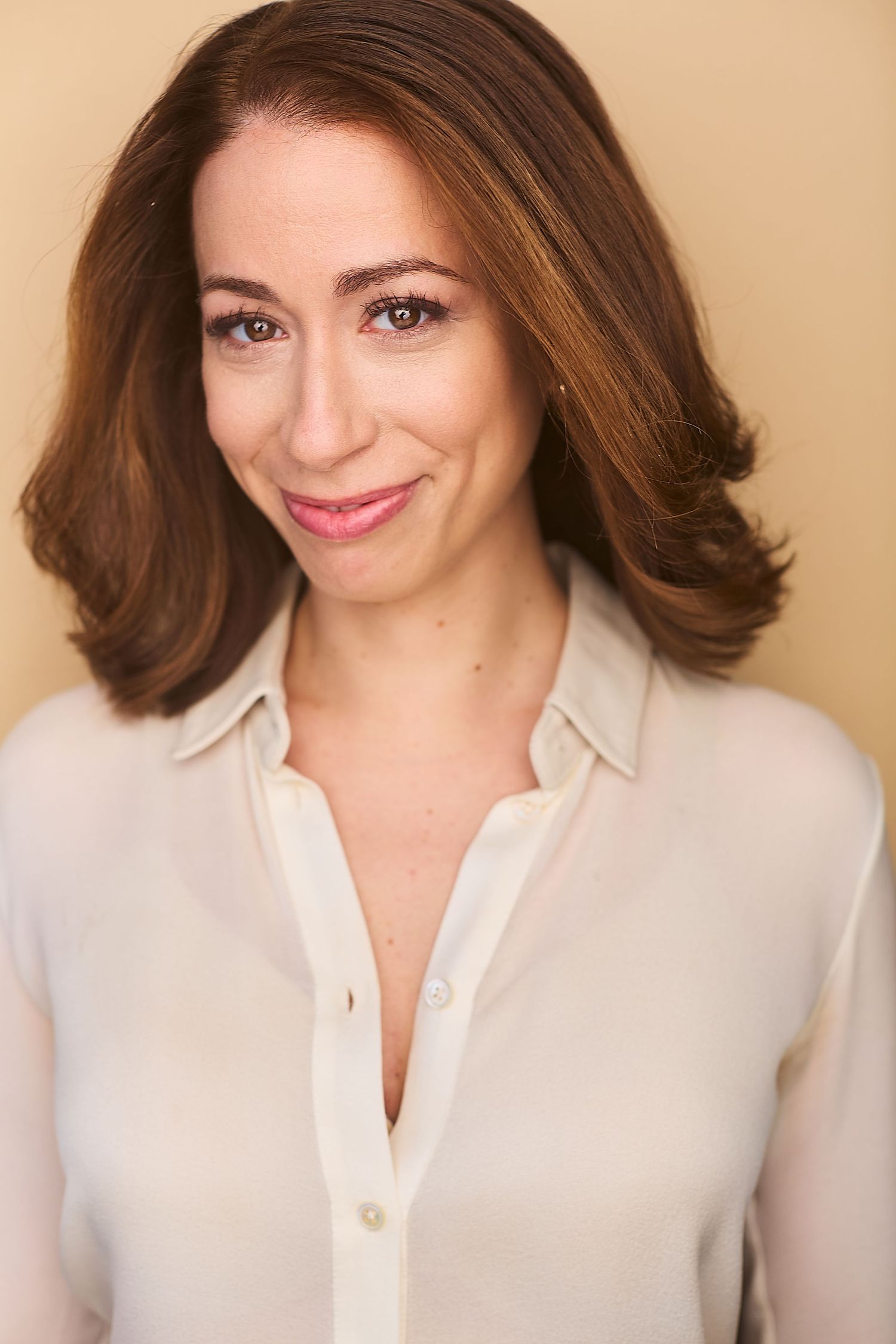 Corporate NYC headshot of a woman in a beige blouse against a tan background.