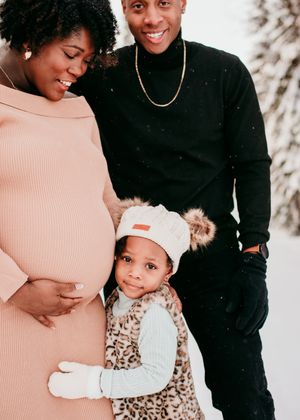 Expecting parents standing with their young child outdoors during a maternity session