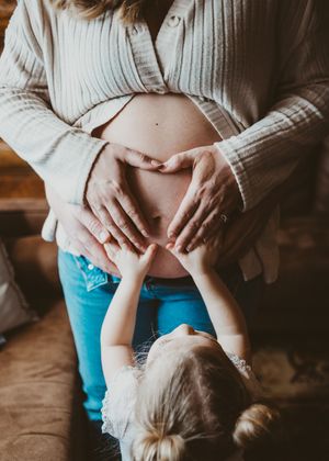 Pregnant mother standing with her young child touching her belly during a maternity session