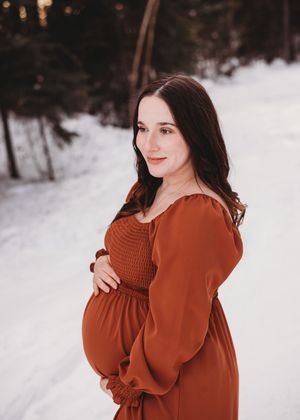 Pregnant woman standing outdoors in a snowy winter setting during a maternity session