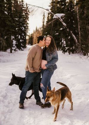 Couple standing together with their dogs in a snowy forest during an outdoor portrait session