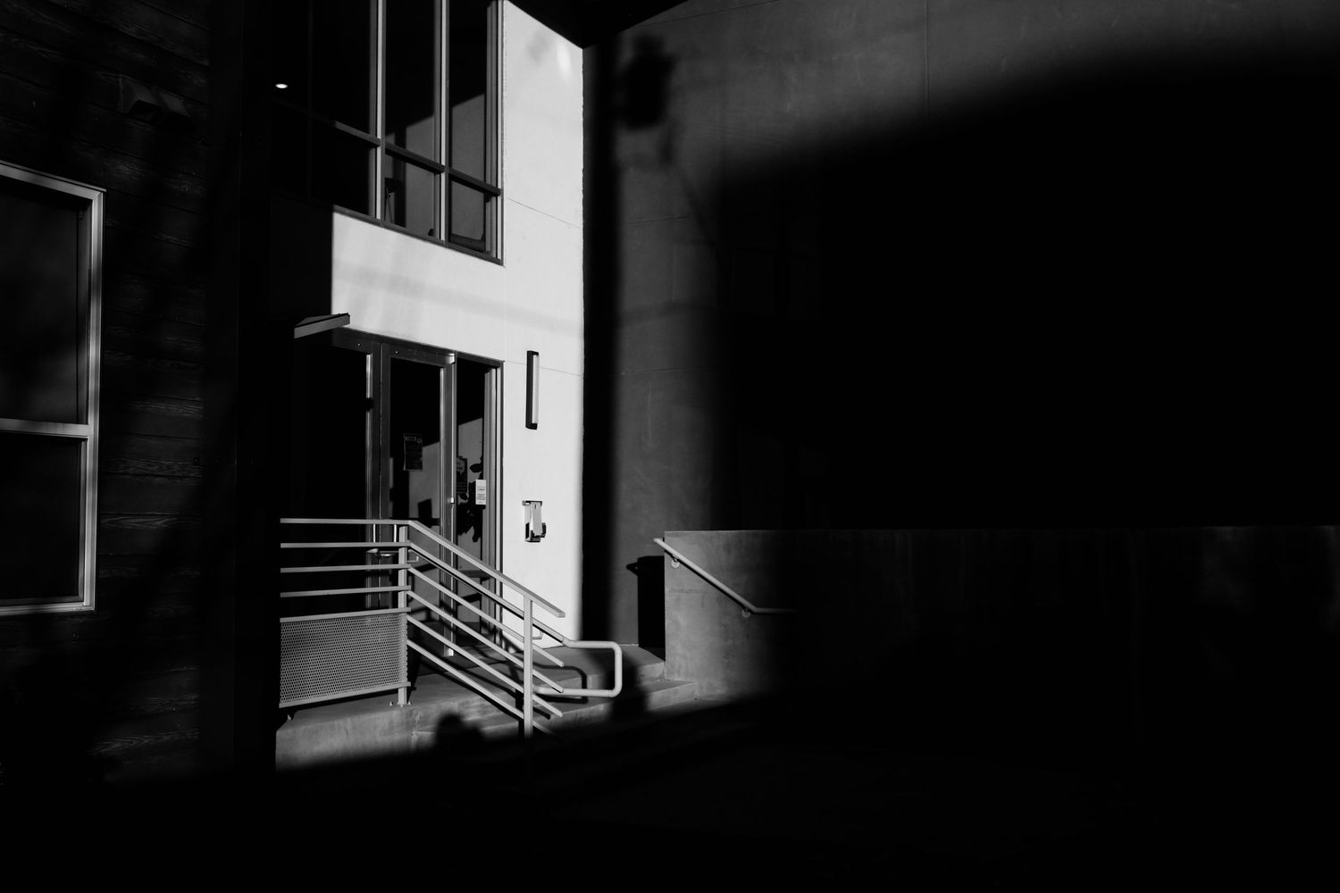 Black and white photo of a dimly lit building entrance with metal railings and steps at night.