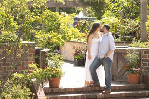 Couple shares a tender kiss on brick garden steps surrounded by lush greenery and colorful flowers.
