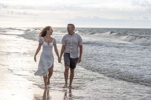 Romantic couple walking hand in hand barefoot along a scenic beach at golden sunset.