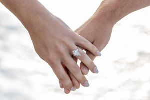 Close-up of couple holding hands showing a stunning diamond engagement ring on the beach.