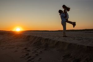 Man lifting woman at sunset on a sandy beach in silhouette.