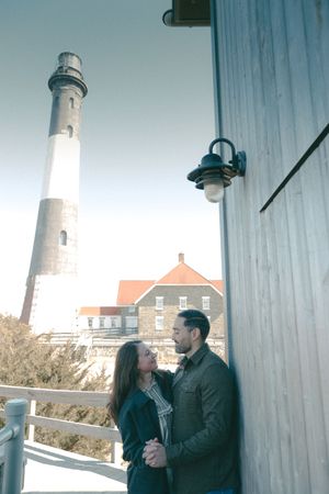 Couple sharing a romantic moment near a historic lighthouse and brick building on a clear day.