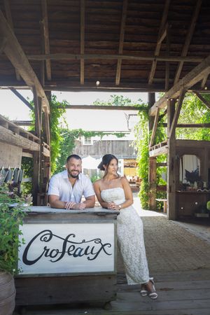 Smiling couple posing together at a rustic wooden bar counter with a Croteaux sign in a vineyard.