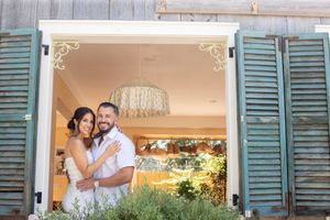 Happy couple embracing in a charming doorway with teal shutters and a chandelier inside.