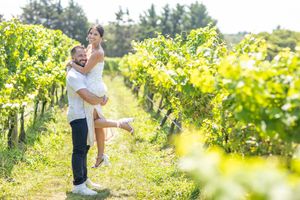 Joyful couple embracing in a sunny vineyard with lush green grapevines in the background.