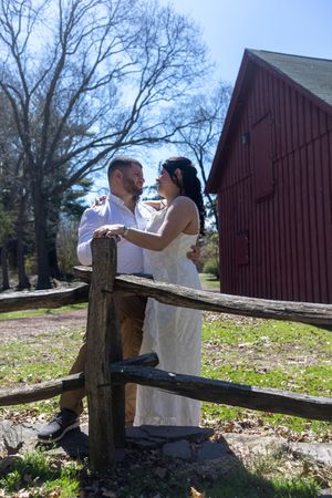 Couple sharing a romantic moment by a wooden fence near a red barn.