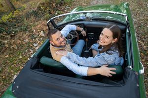 Couple laughing together while relaxing inside a vintage green convertible car outdoors.
