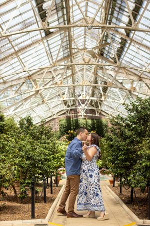 Couple sharing a romantic kiss inside a stunning glass greenhouse surrounded by lush greenery.