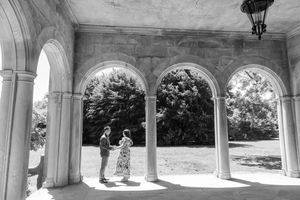 Couple standing under elegant stone arches in black and white photo.