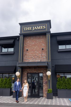 Elegant couple walks hand-in-hand outside The James restaurant with dark exterior and brick facade.