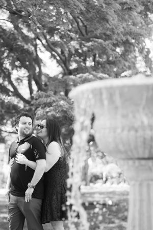 Couple embracing near a stone fountain in a park, black and white.